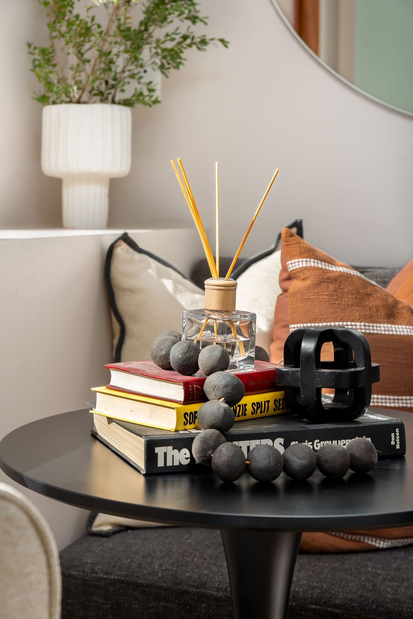 Side table styled with books, a reed diffuser and a black sculpture