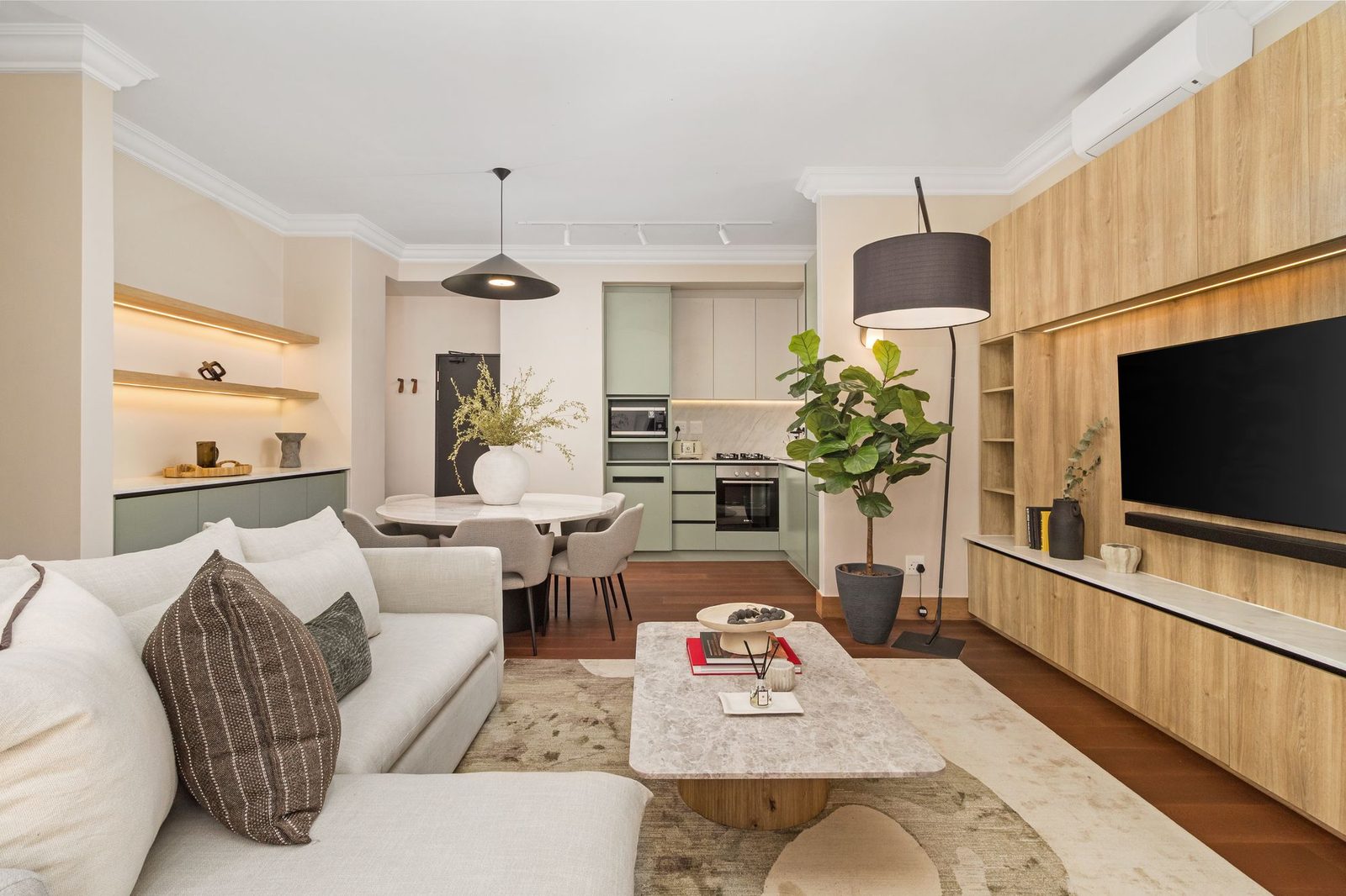 Open-plan living room with an oak media wall and a sage green kitchen