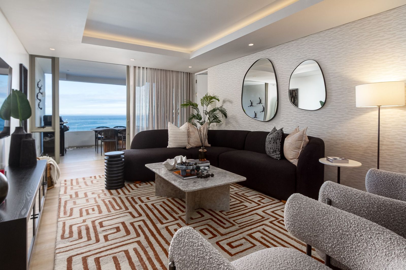Living room with a curved dark sofa, pebble-shaped mirrors and a patterned rug