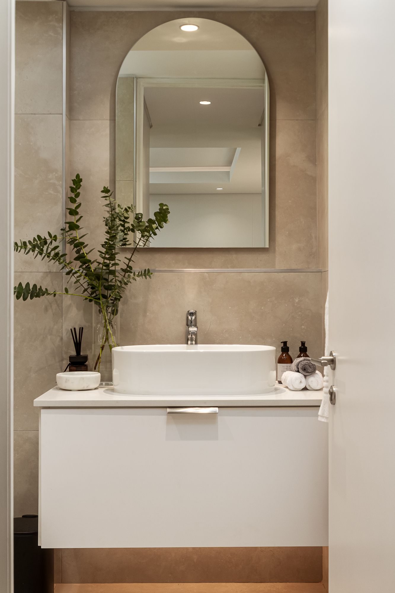 Bathroom with an arched mirror, stone-look tiles and a white floating vanity