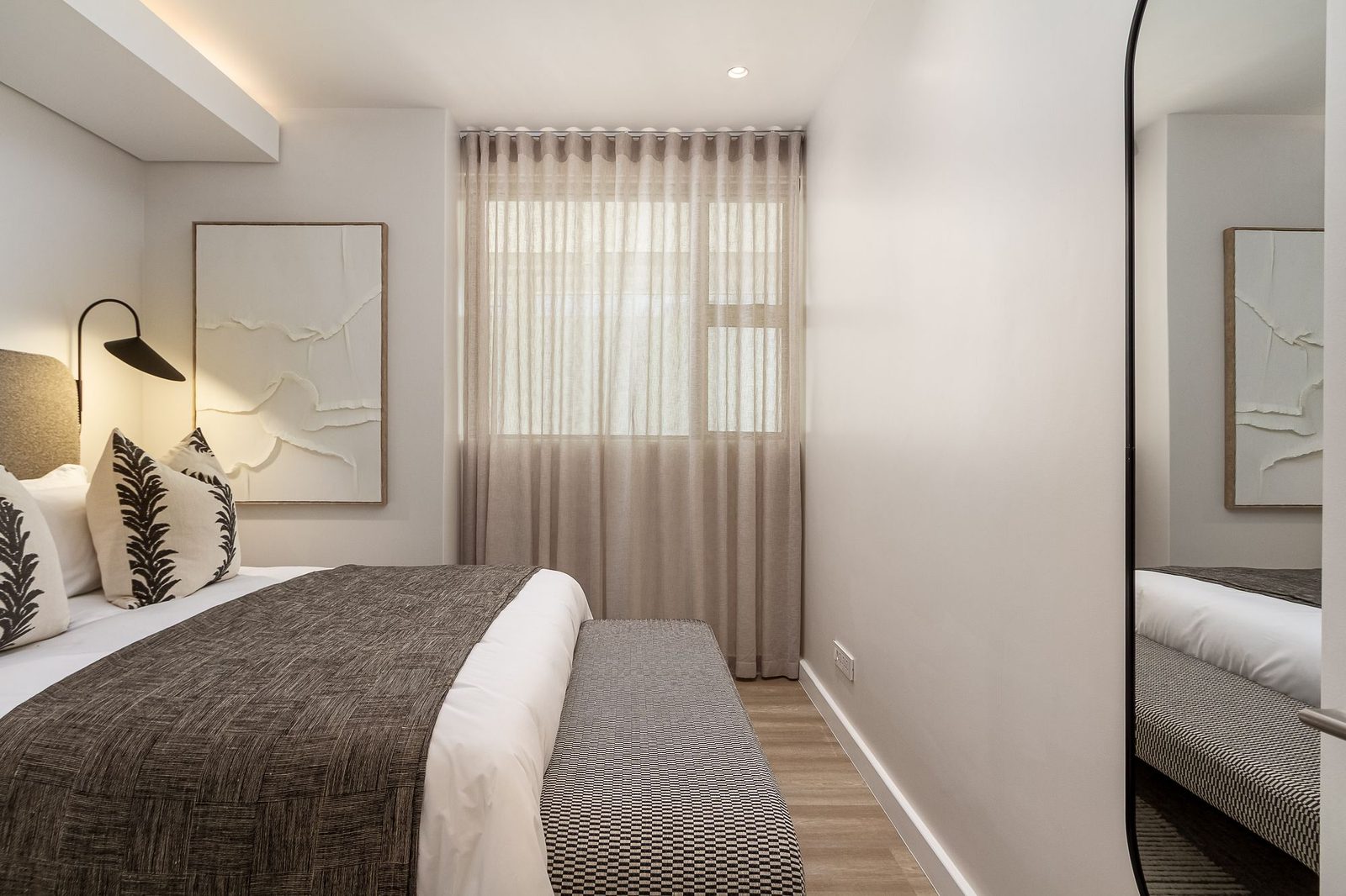 Bedroom with a sheer linen curtain, textured artwork and a woven bench