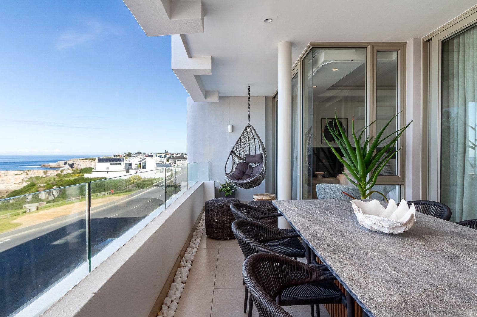 Balcony with a hanging egg chair, woven poufs and a view along the coast